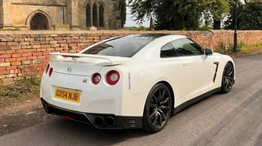 White Nissan GTR R35 parked outside a church, side angle view highlighting sporty design and wedding setting.