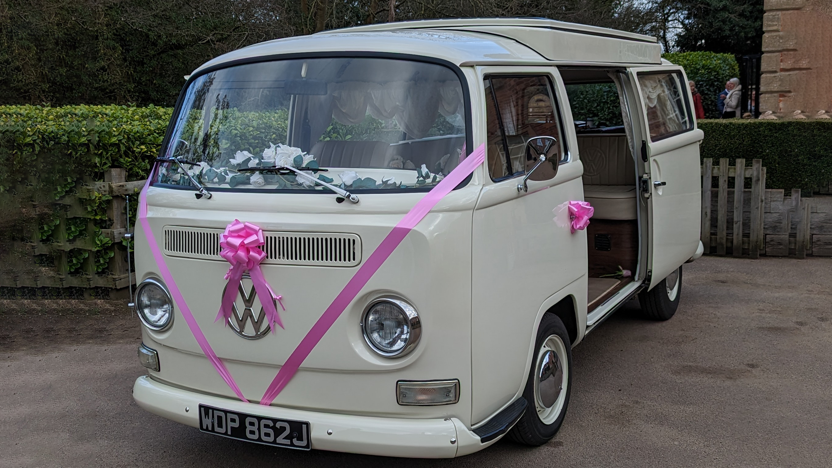 Old English White campervan front view with pink wedding ribbons and bows, doors closed, parked outside venue