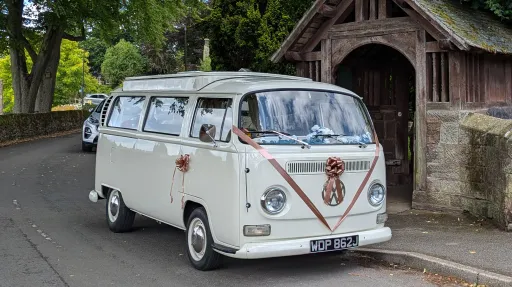 Classic campervan baywindow parked outside a church dressed with amber coloured ribbons and bows