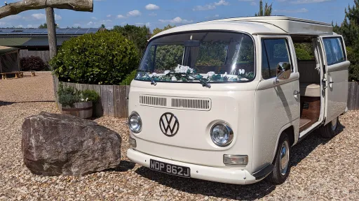 Classic cream VW campervan left side view with sliding door open showing cream seating, no ribbons, parked on gravel drive