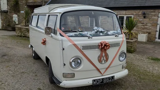 Classic VW campervan front view with ribbon and bow on grille, doors closed, parked near venue entrance