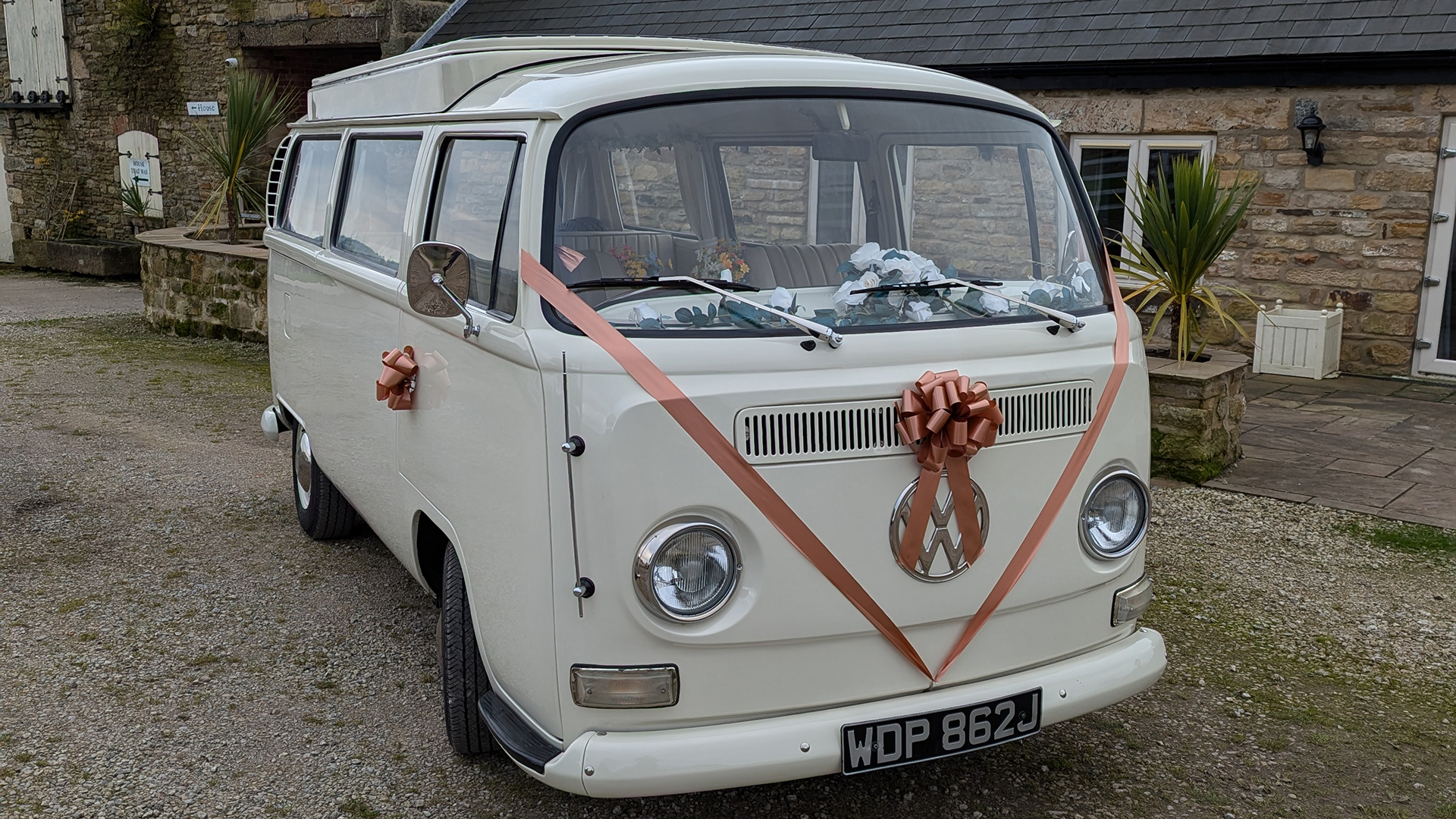 Classic VW campervan front view with ribbon and bow on grille, doors closed, parked near venue entrance