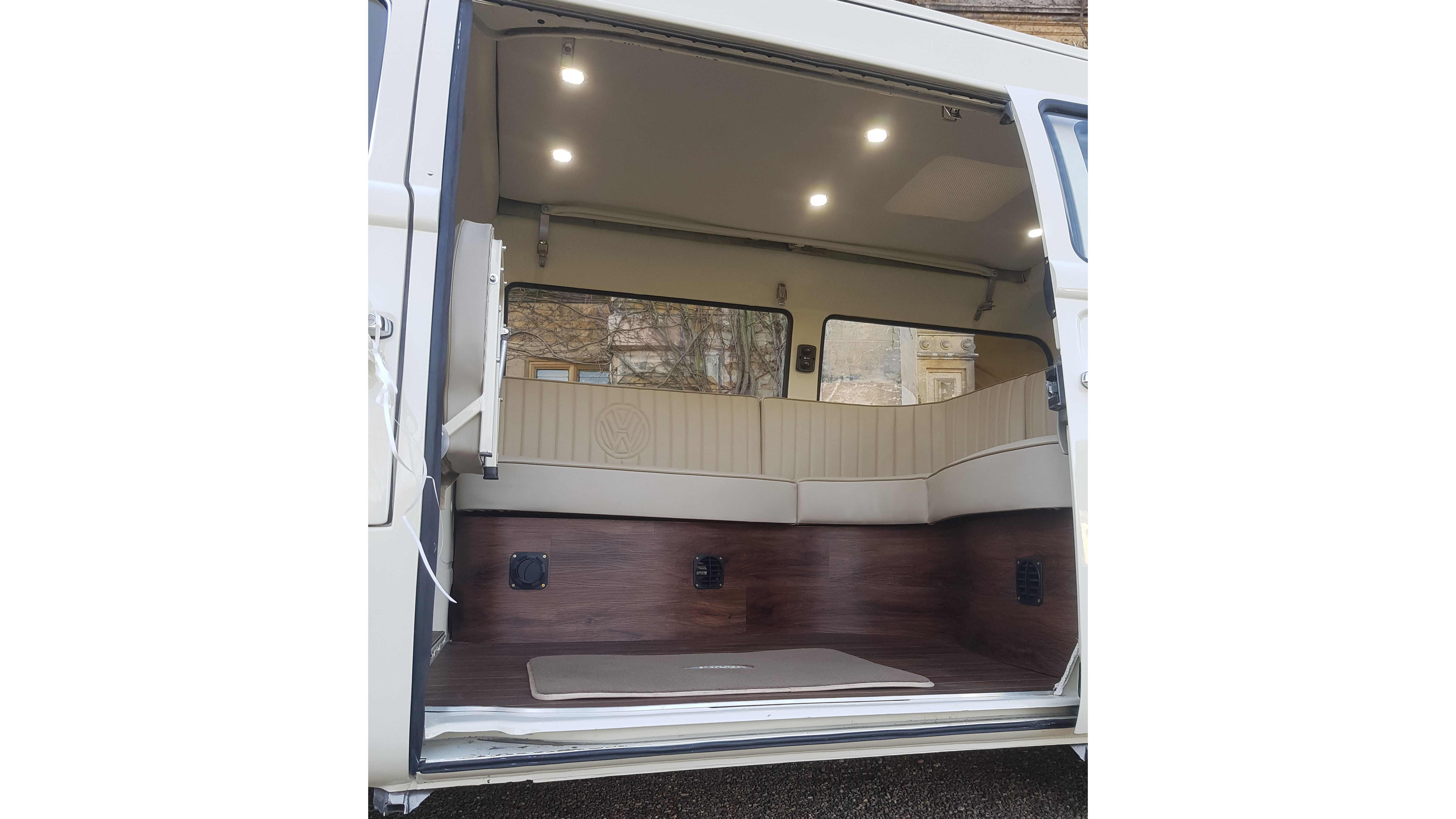 VW campervan rear interior view showing cream seating layout and wooden floor, doors open