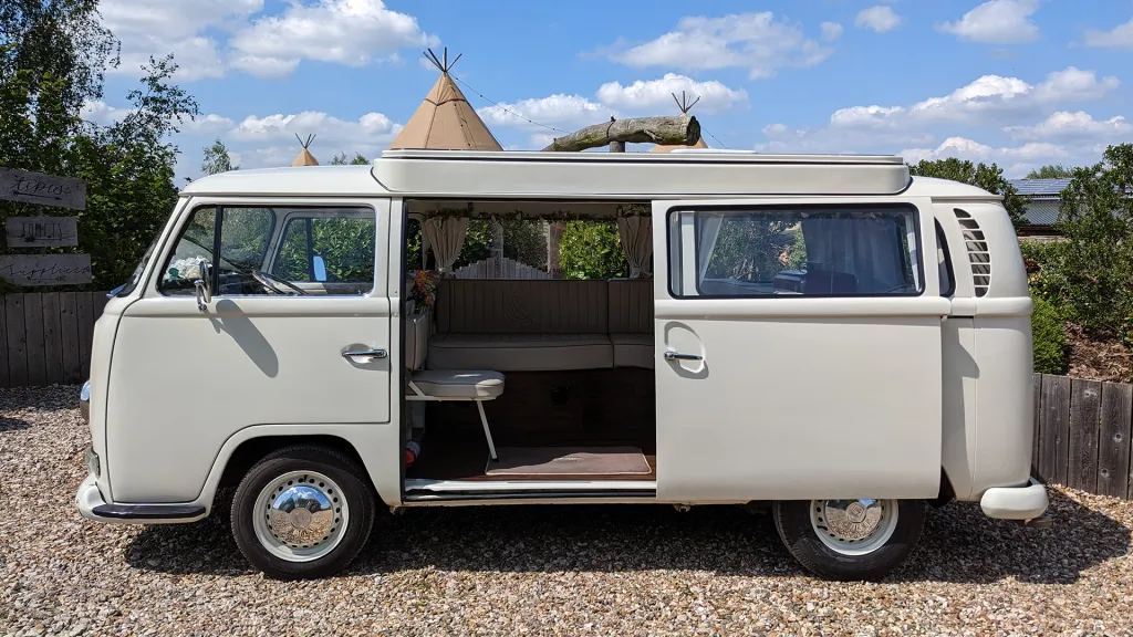 Classic VW campervan left side view with sliding door open, cream interior visible, parked on gravel