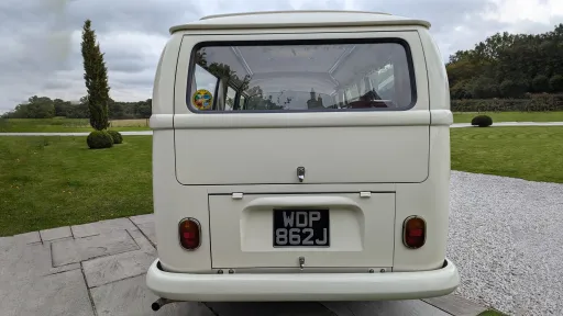 VW campervan rear view, doors closed, cream interior visible through windows, parked on lawn