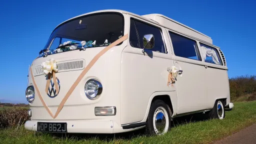 Classic VW campervan front angle with wedding ribbons and bows on grille, doors closed, parked at venue