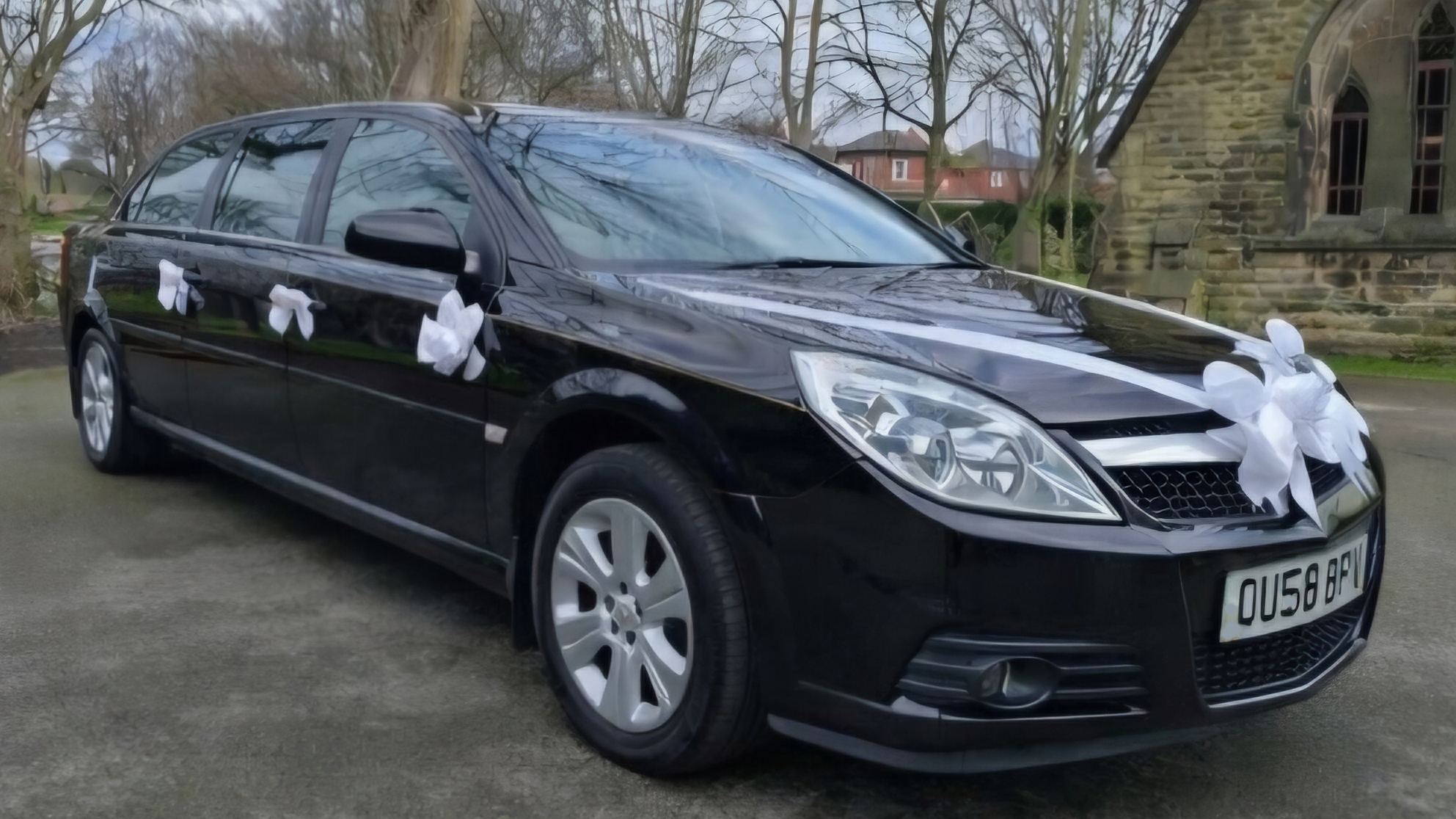 Black 7-seater stretched Vauxhall Vectra limousine for hire decorated with white wedding ribbons and bows on door handles