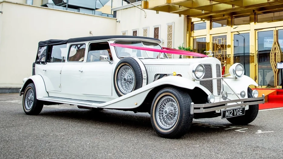 White Beauford Landaulette wedding car decorated with pink ribbons parked outside venue entrance