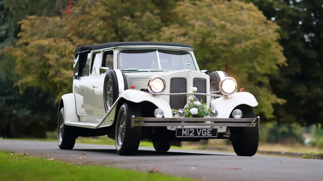 Right front angle white Beauford Landaulette limousine at wedding venue with greenery background