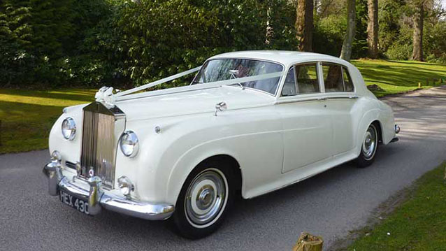 Front three quarter view of 1959 Rolls-Royce Silver Cloud in Old English White with chrome grille on driveway