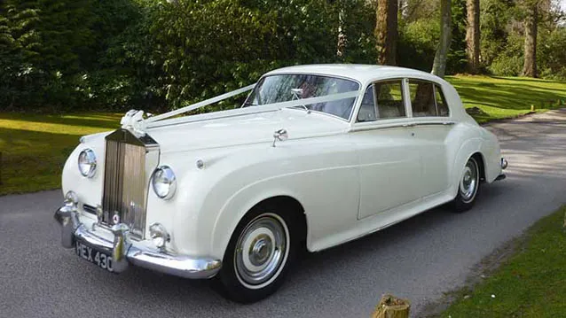 Front three quarter view of 1959 Rolls-Royce Silver Cloud in Old English White with chrome grille on driveway