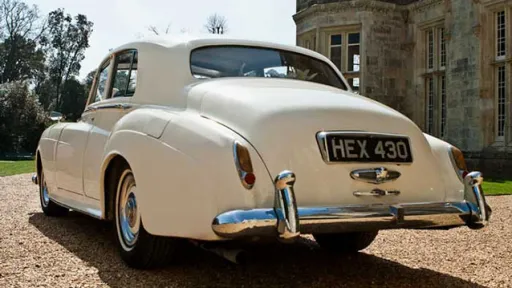Rear view of 1959 Rolls-Royce Silver Cloud in Old English White parked on gravel driveway outside stone venue