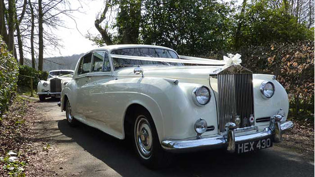 Side profile of 1959 Rolls-Royce Silver Cloud in Old English White parked on garden driveway with trees