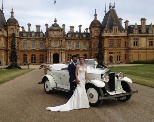 A white Vintage Rolls-Royce with Bride and Groom holding each other standing in front of the wedding car