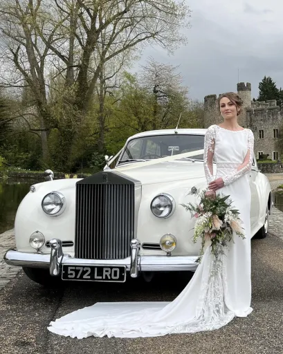 Bride holding a bouquet of flower and wearing a white wedding dress standing in front of a classic Rolls-Royce Silver Cloud at a Manchester wedding venue