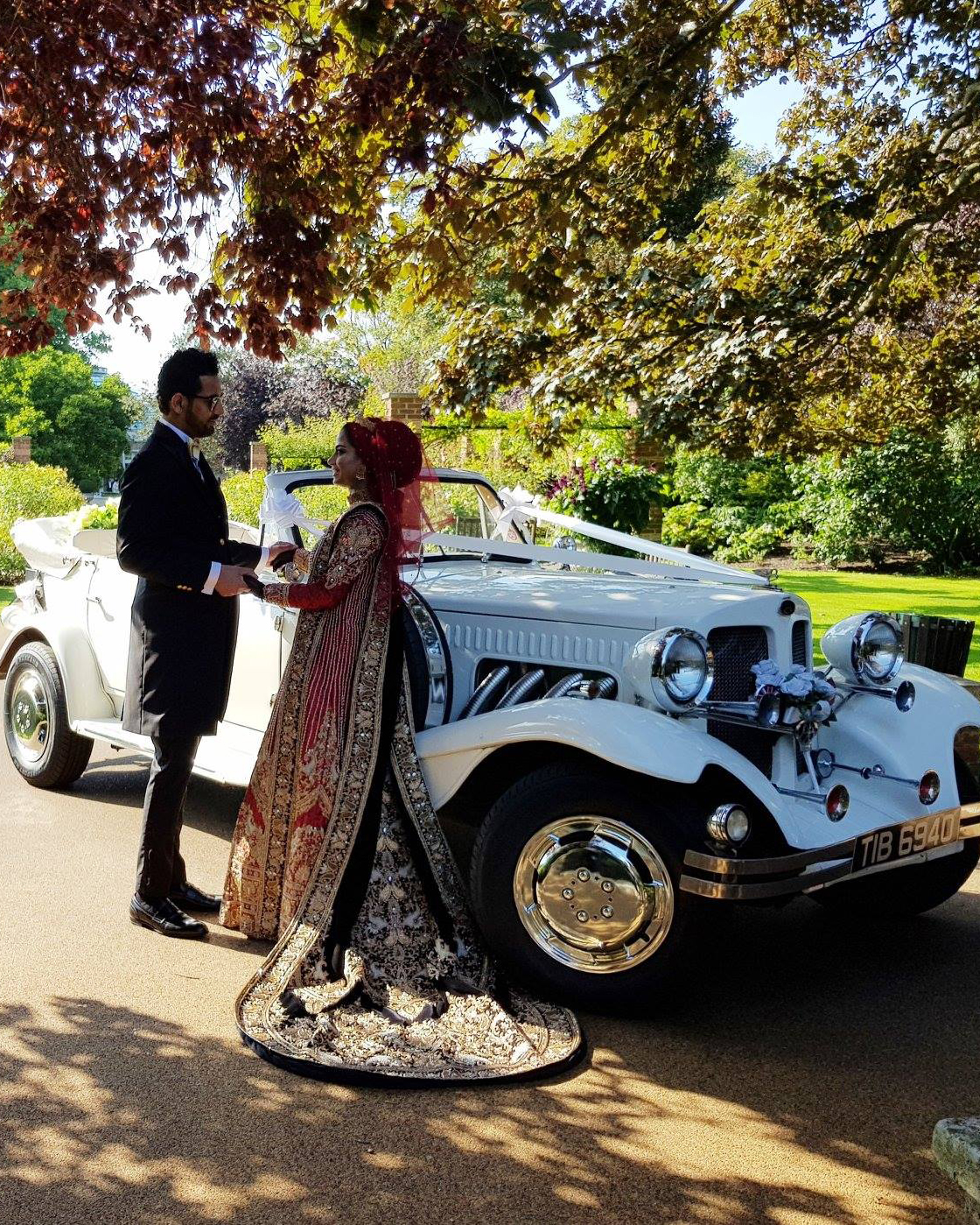 Asian Couple standing in front of a fully convertible vintage Beauford in White with greenery in the background