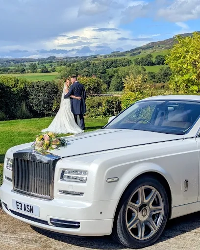 Modern White Rolls-Royce Phantom with a colourful bouquet of flower on the bonnet and happy couple in the far background posing for photos.