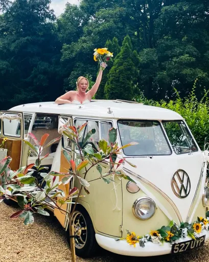 Retro classic Volkswagen Campervan decorated with wedding flowers and bride holding a bouquet of flower cheering.