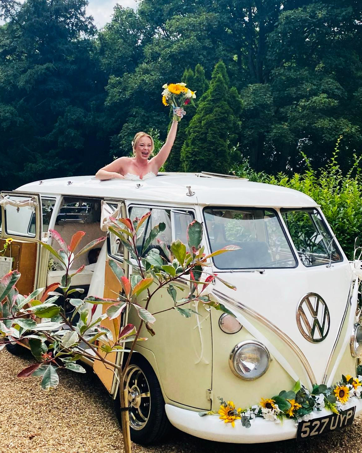 Retro classic Volkswagen Campervan decorated with wedding flowers and bride holding a bouquet of flower cheering.