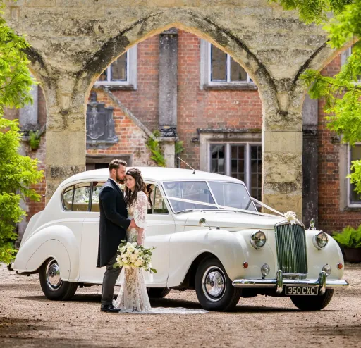 Classic 7-seater Austin Princes Limousine in Ivory with Bride and Groom holding each other’s ion front of the vehicle
