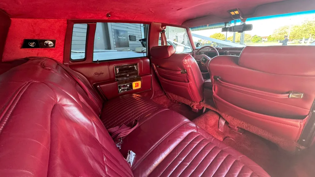 1990 Cadillac Brougham burgundy red leather rear interior, plush bench seating, classic American luxury finish.