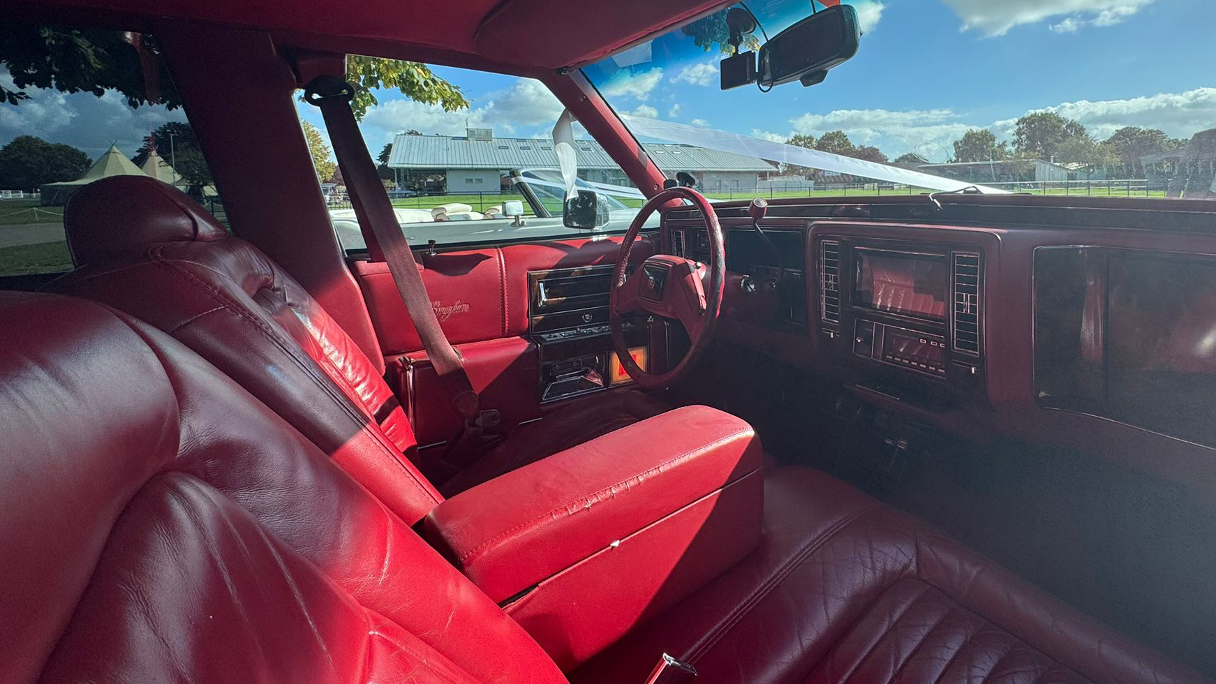 1990 Cadillac Brougham front cabin, burgundy red leather bucket seats, chrome dashboard trim, classic American interior.