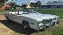 Front right angle of white Cadillac Eldorado convertible from 1975 with open top roof, chrome detailing and alloy wheels at countryside wedding location in East Anglia