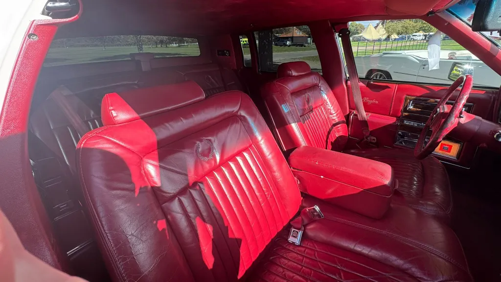 1990 Cadillac Brougham burgundy red leather interior, rear cabin angle, chrome accents, deeply cushioned seating.