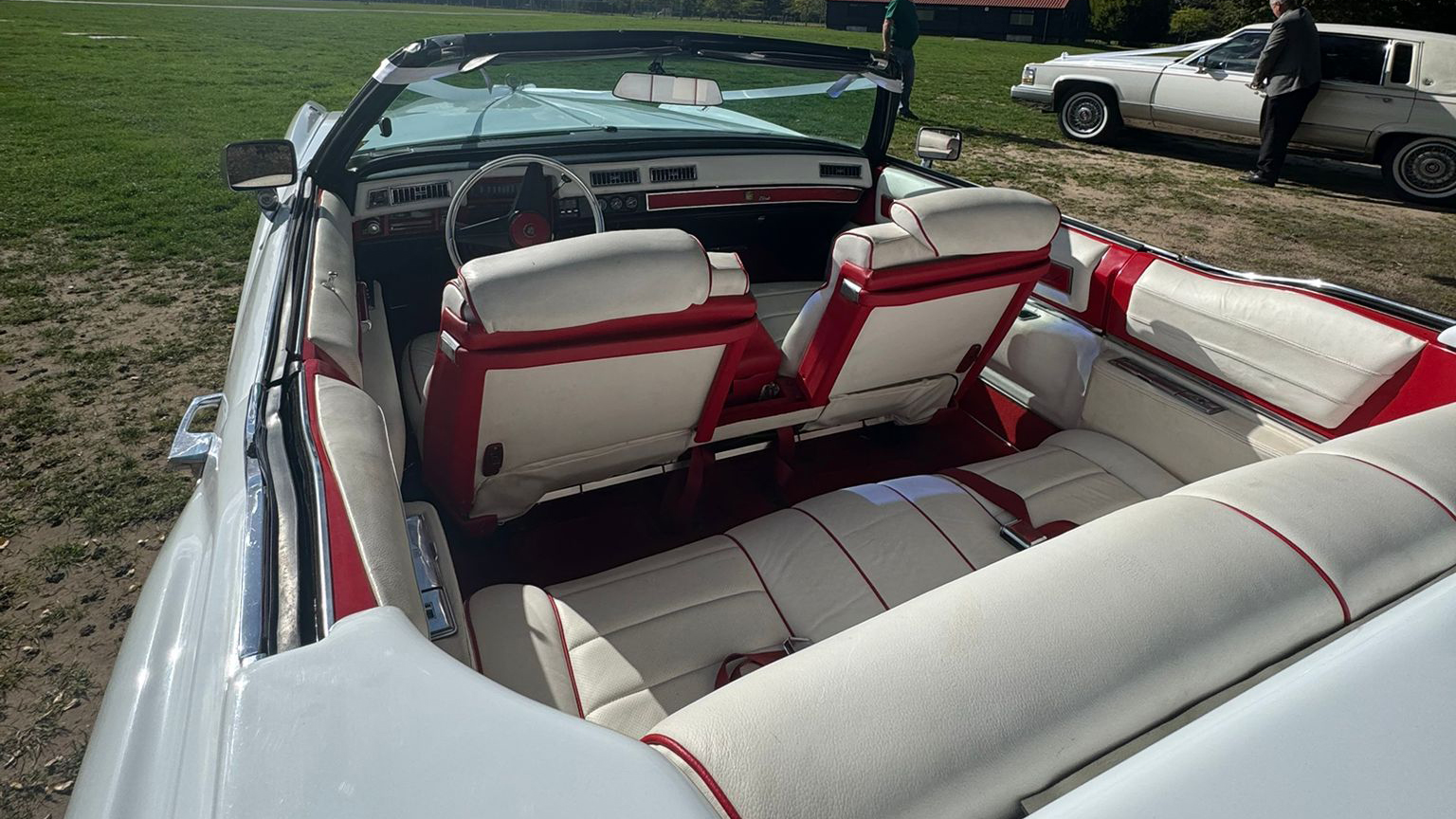 Rear seating area inside a 1975 Cadillac Eldorado convertible with white and burgundy leather seats and open roof under sunny skies