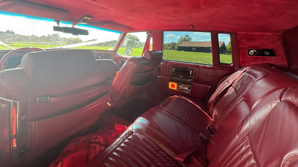 1990 Cadillac Brougham spacious burgundy red leather rear bench seat, classic American chauffeur-driven interior.