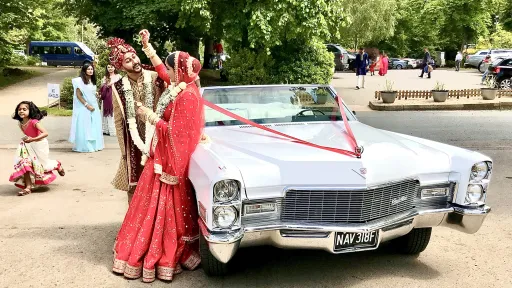 Bride and groom standing by a classic Cadillac Convertible dressed with Red Ribbon