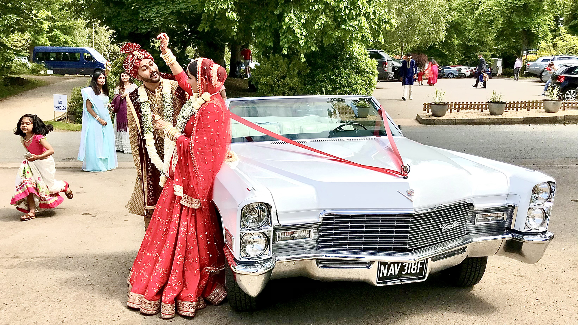 Bride and groom standing by a classic Cadillac Convertible dressed with Red Ribbon