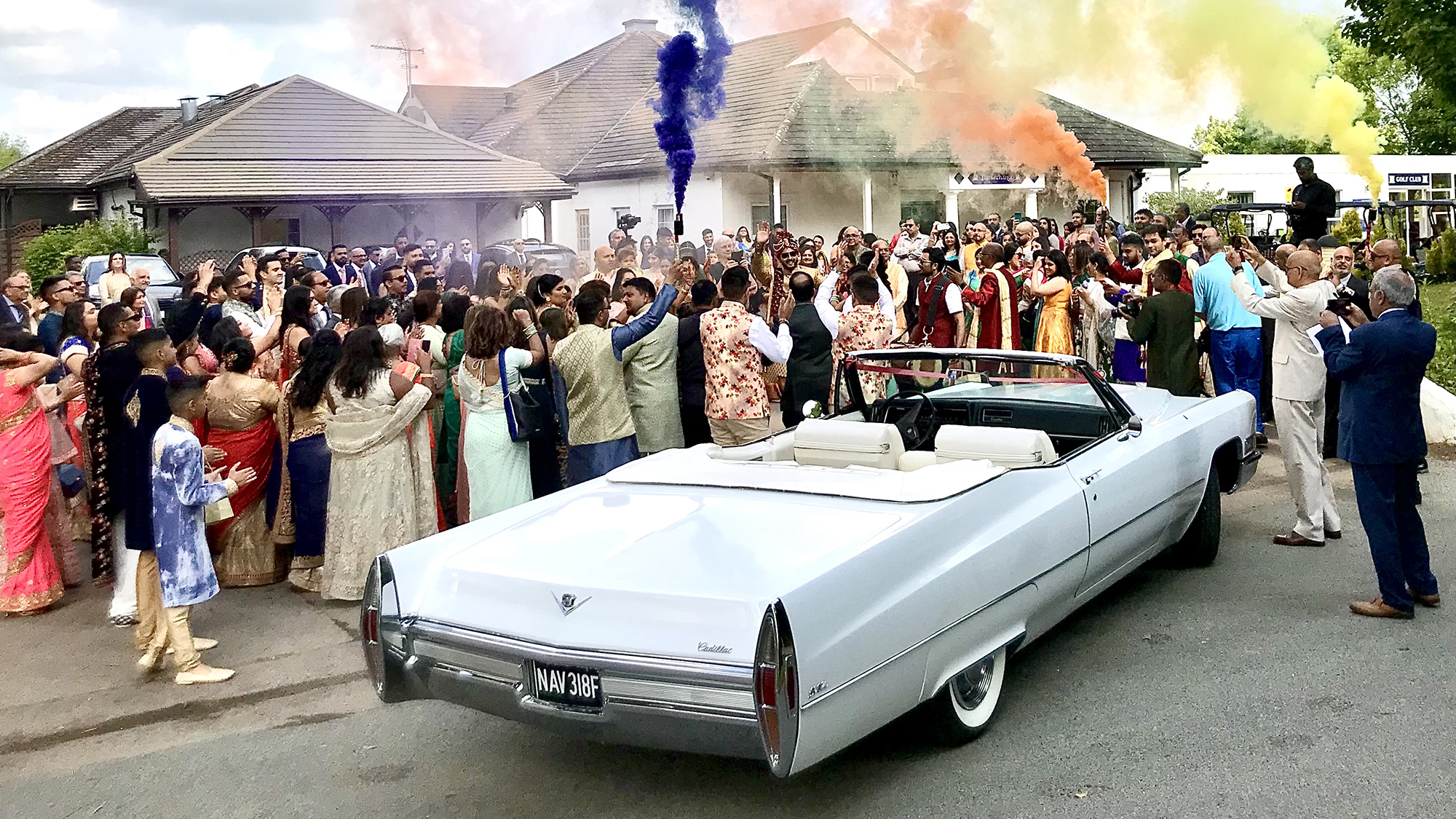 Classic White Convertible Cadillac at an Asian Wedding with wedding guests around the vehicle setting off multi coloured smoke flairs