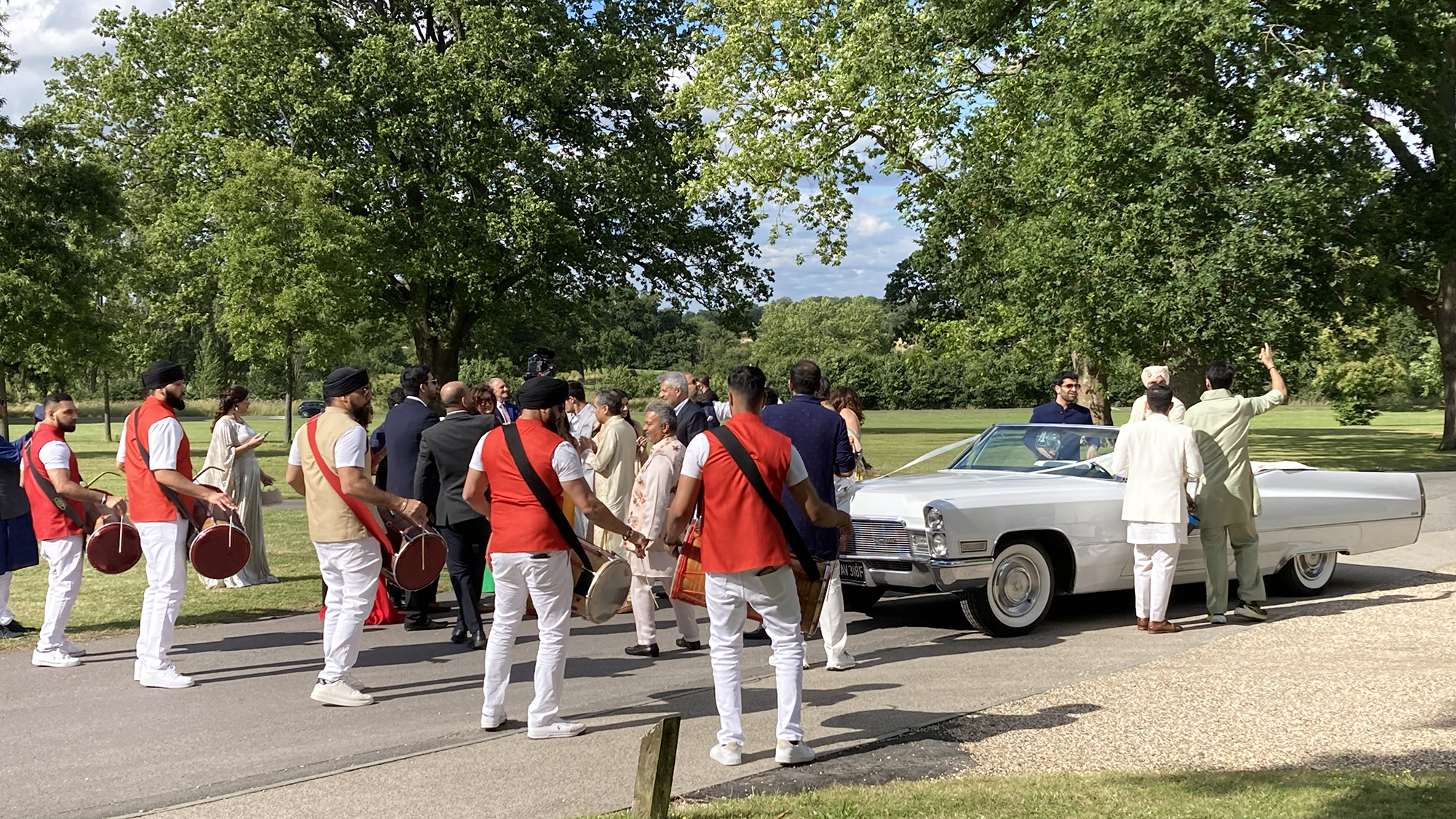 Asian Groom Barat antrance in a classic White Cadillac convertible with drummers in front of the vehicle