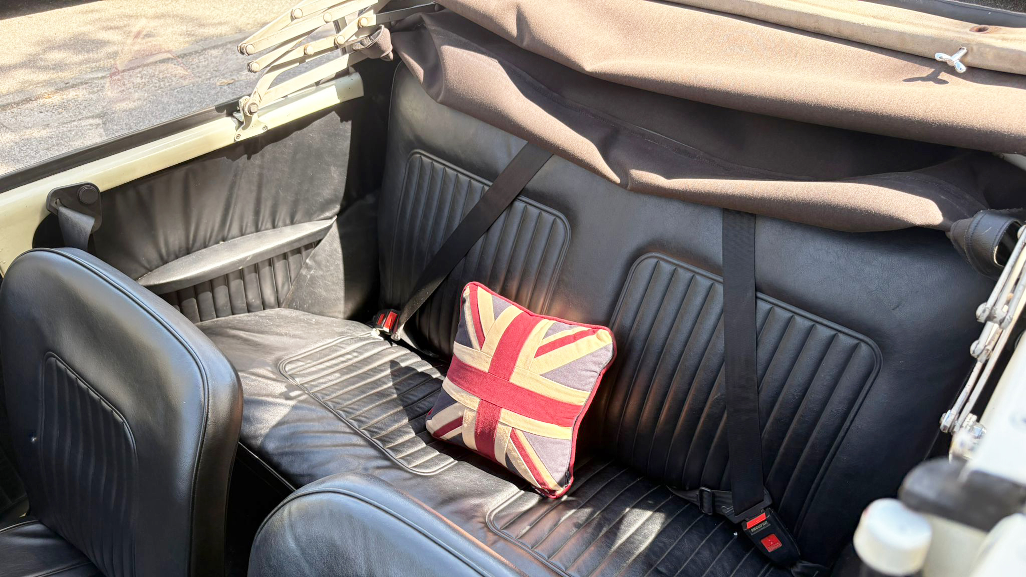Black leather rear seating inside a classic Morris Minor Convertible wedding car with Union Jack cushion and folded convertible roof visible.
