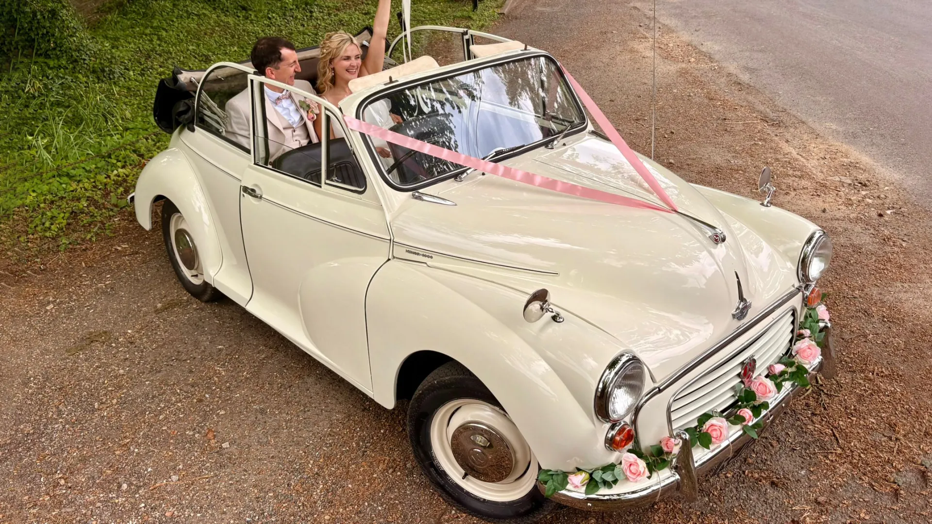 Front side view of a 1969 Morris Minor Convertible wedding car in Old English White with pink ribbons and floral bonnet decoration in Kent.