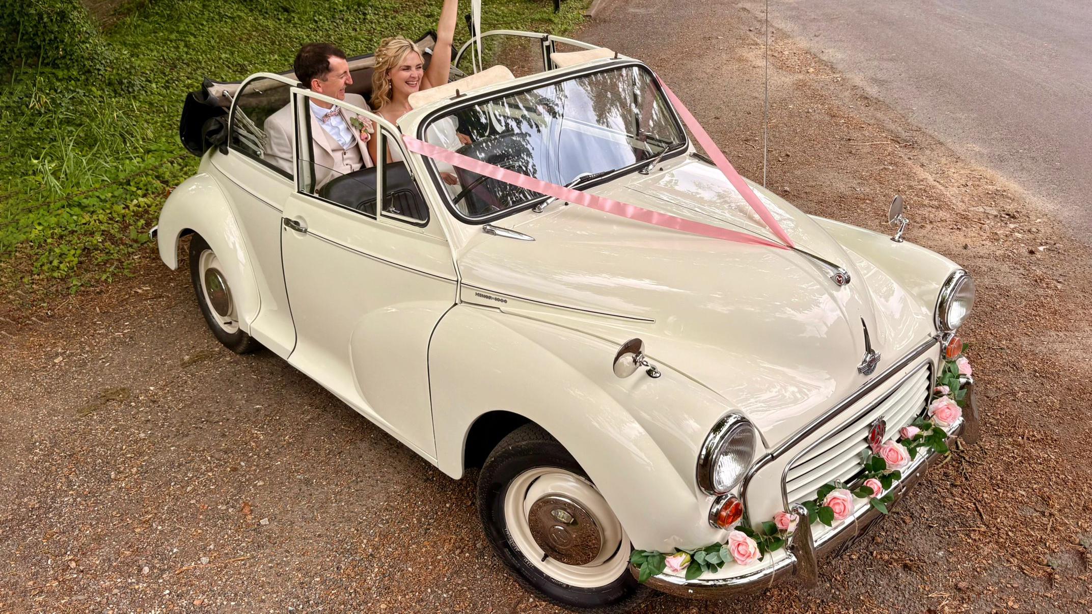 Front side view of a 1969 Morris Minor Convertible wedding car in Old English White with pink ribbons and floral bonnet decoration in Kent.