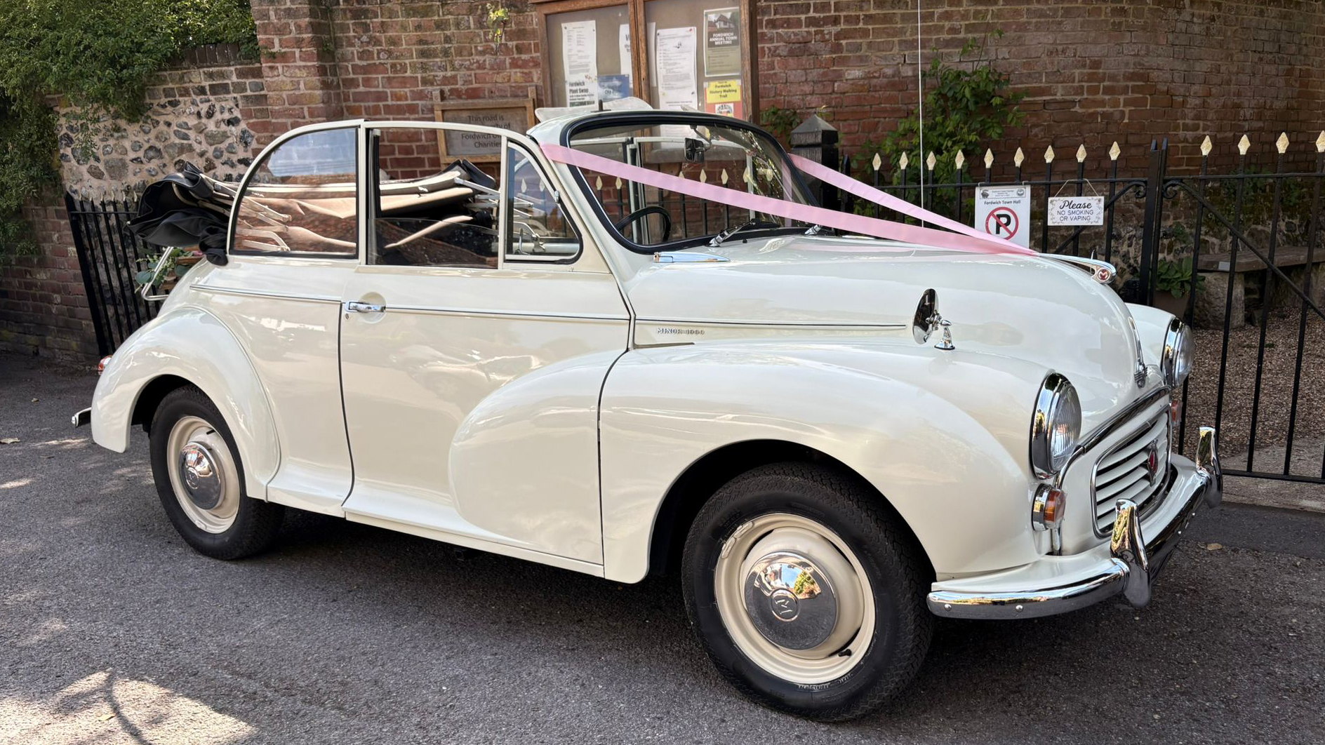 Classic Morris Minor Convertible parked outside a wedding venue in Kent, finished in Old English White with chrome hubcaps and black folding roof.