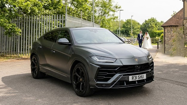 Grey Lamborghini Urus parked outside a wedding venue with matte grey paint, black alloy wheels and tan orange leather interior visible through the windows