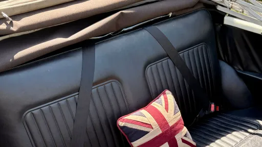 Close up of black leather seats inside a vintage Morris Minor Convertible wedding car with soft top roof folded back.