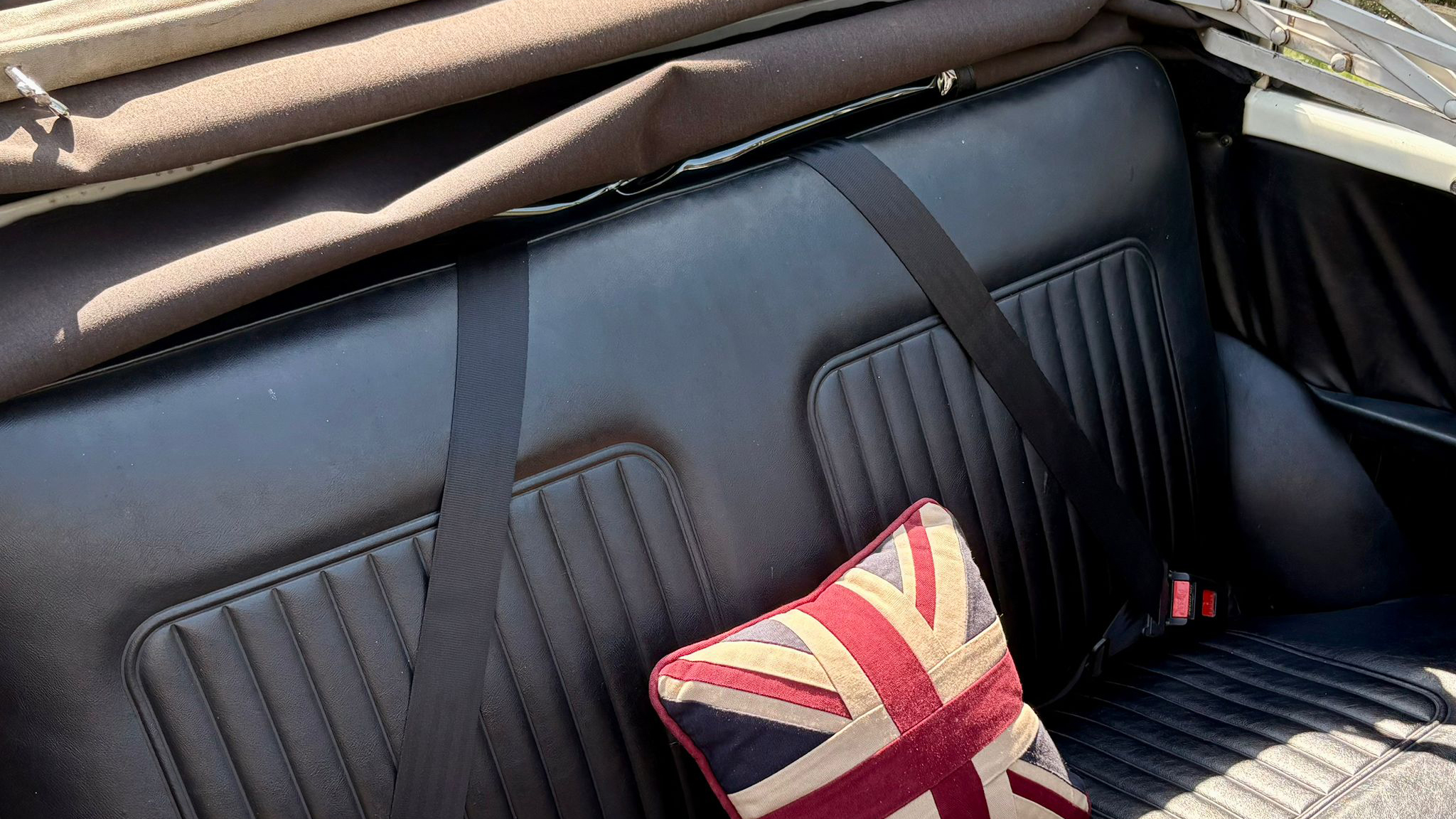 Close up of black leather seats inside a vintage Morris Minor Convertible wedding car with soft top roof folded back.