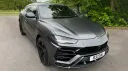 Three quarter front view of a grey Lamborghini Urus luxury SUV with matte finish, black styling pack and tinted windows