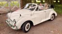 1969 Morris Minor Convertible wedding car driving through a countryside venue in Kent with bride and groom smiling from the rear seats.
