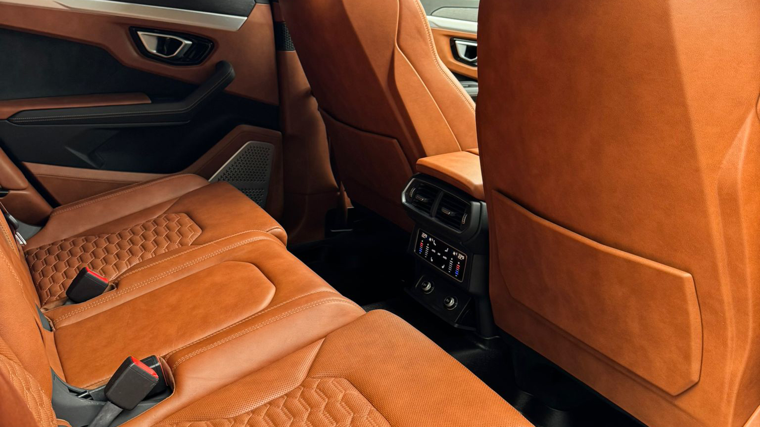 Rear passenger seating inside Lamborghini Urus with tan orange leather seats, stitched detailing and luxury rear cabin controls