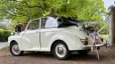 Rear side view of a Morris Minor Convertible wedding car decorated with pink ribbons and floral arrangement on the luggage rack.