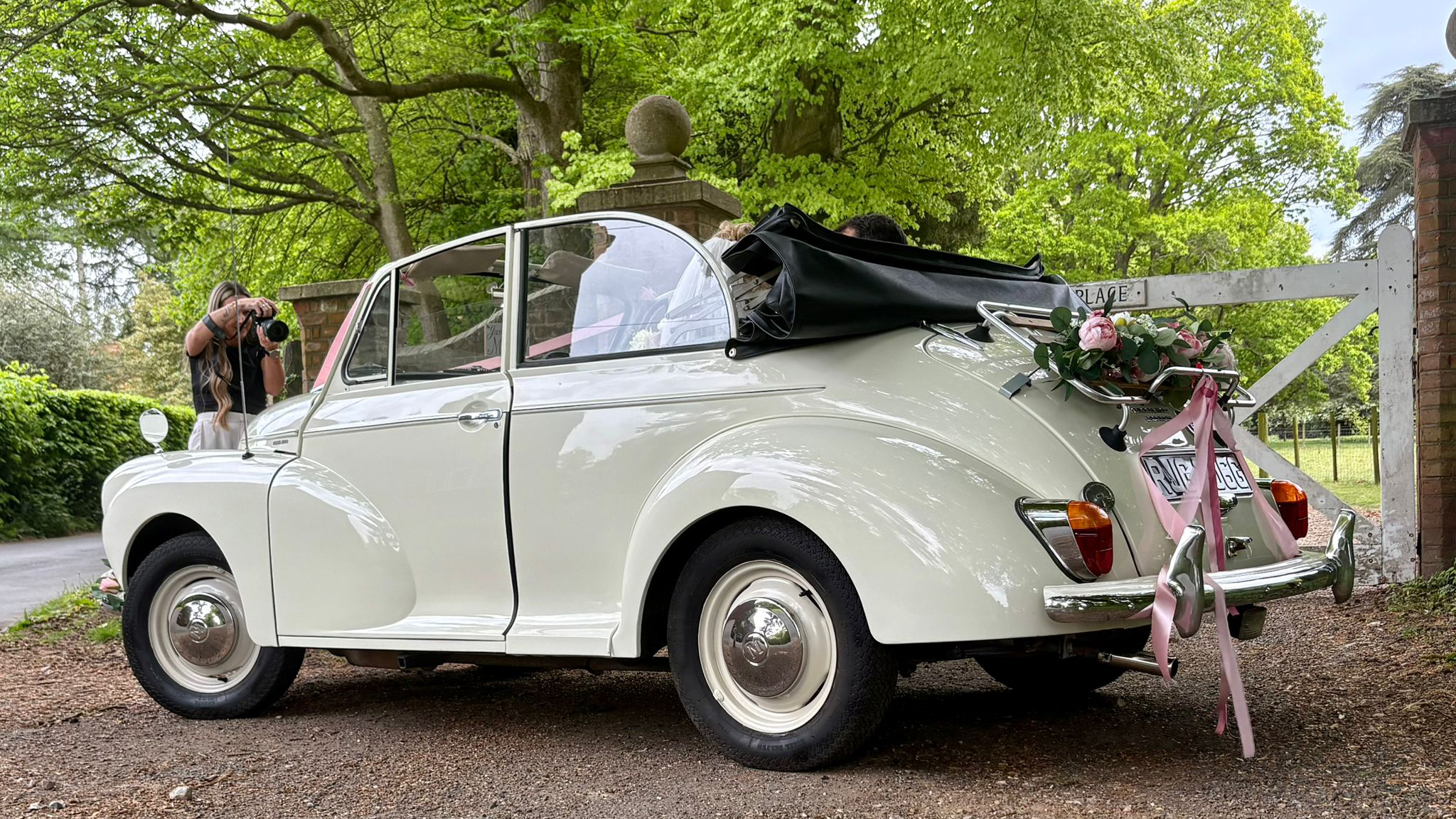 Rear side view of a Morris Minor Convertible wedding car decorated with pink ribbons and floral arrangement on the luggage rack.