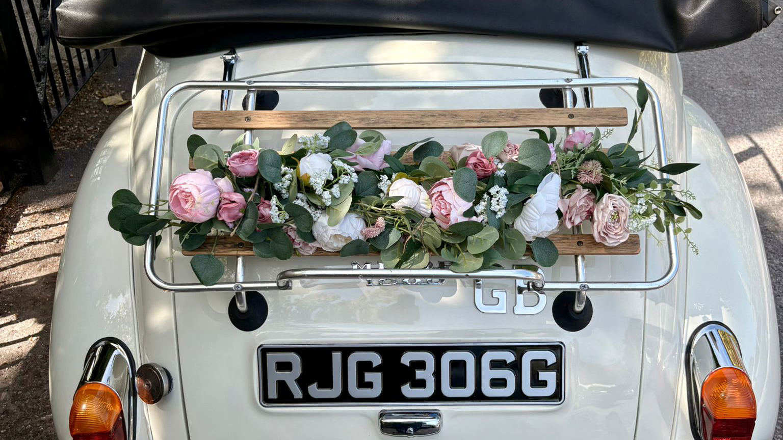 Floral wedding arrangement displayed on the rear luggage rack of a 1969 Morris Minor Convertible with chrome trim and classic registration plate.