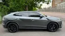 Right side view of grey Lamborghini Urus luxury SUV with sleek coupe styling and black wheels parked near greenery