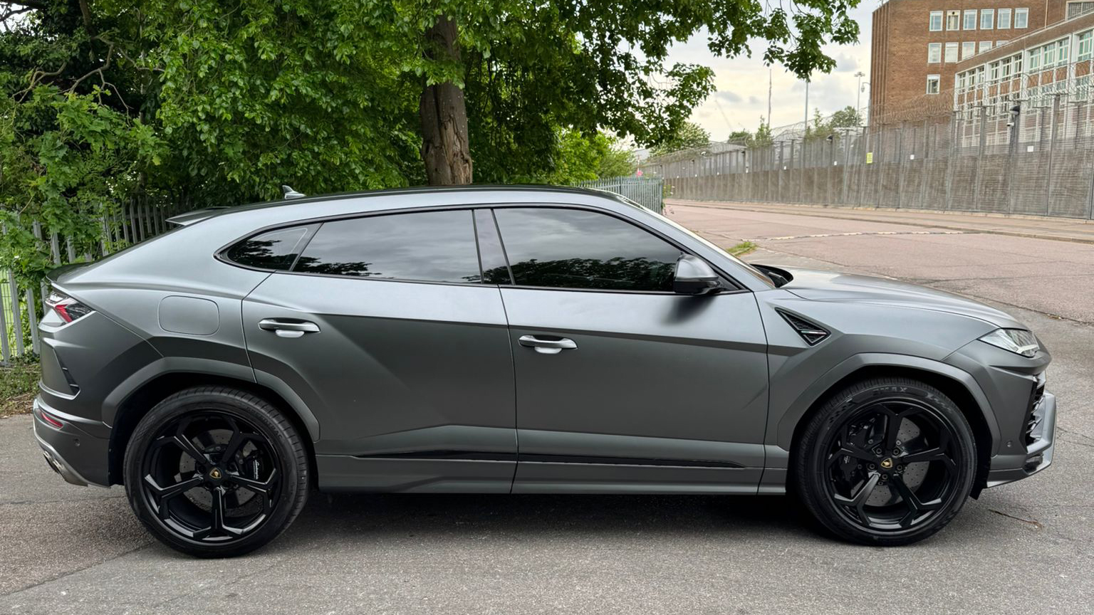 Right side view of grey Lamborghini Urus luxury SUV with sleek coupe styling and black wheels parked near greenery