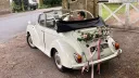 Bride and groom smiling inside a vintage Morris Minor Convertible wedding car with roof down at a countryside wedding location.